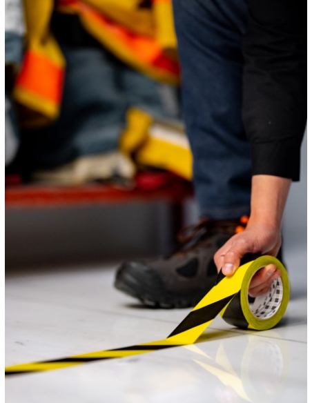 Applicazione manuale dello scotch vinilico 3M™ 766 a bande giallo e nero, per indicazioni di sicurezza.